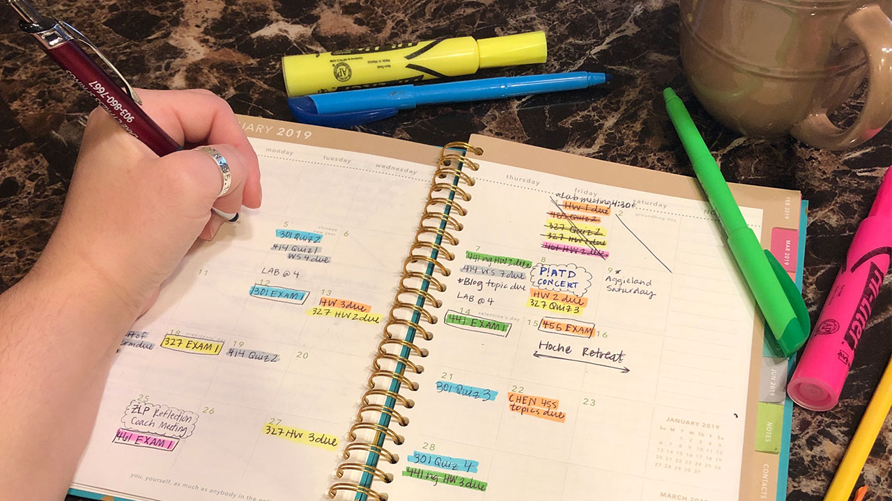 Monthly planner surrounded by highlighters and a cup of coffee.