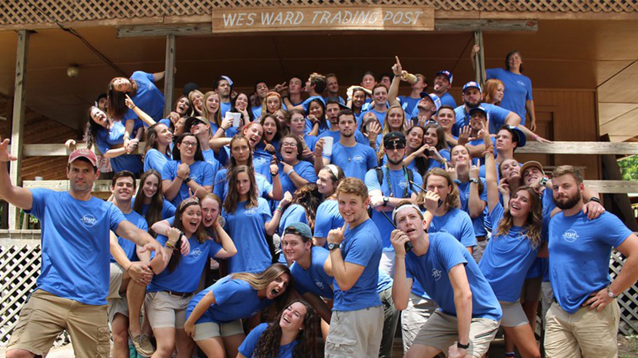 Camp counselors pose in various ways on steps in the same blue shirts.