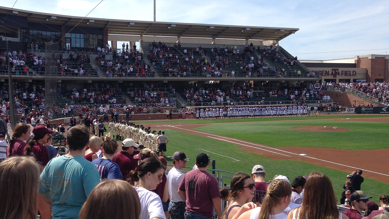 View of Olsen Field from the First Base stands with players lined up during National Anthem.