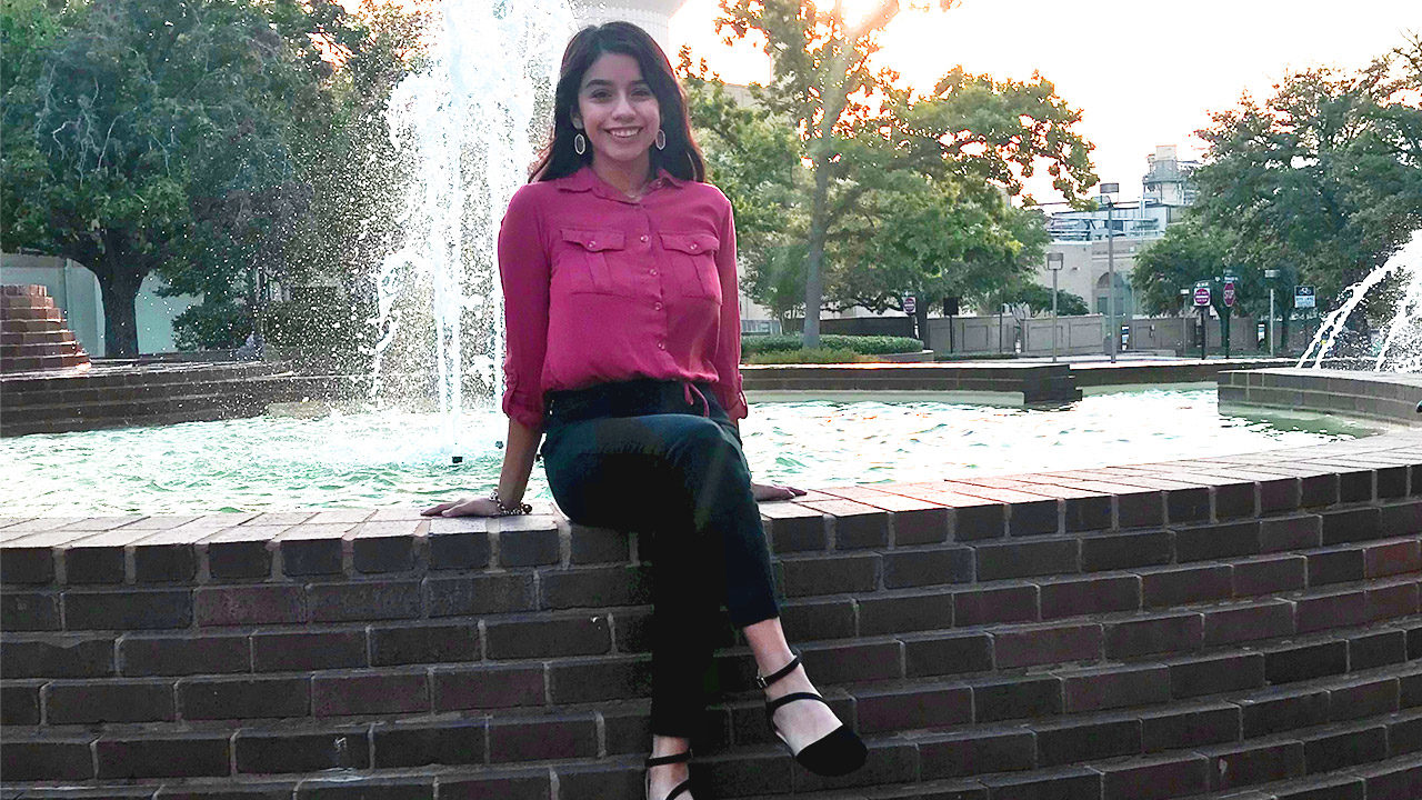 Evelin sitting on the edge of a fountain and smiling.
