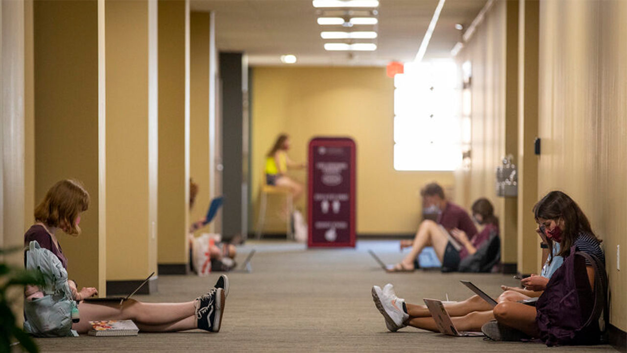 Students in a hallway doing school work on their computers at Texas A&M University