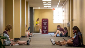 Students in a hallway doing school work on their computers at Texas A&M University