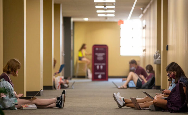 Students in a hallway doing school work on their computers at Texas A&M University