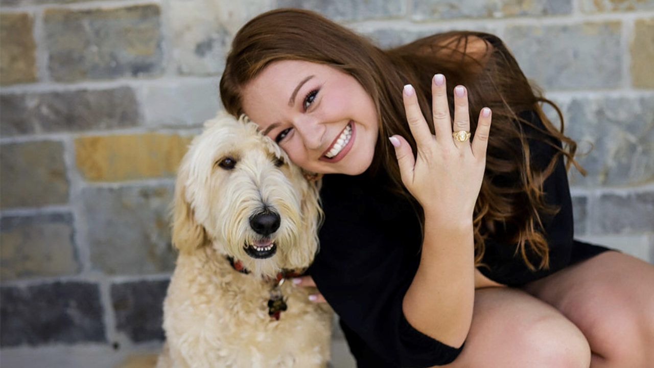 Student Haley showing her Aggie Ring on her hand next to her white fluffy dog