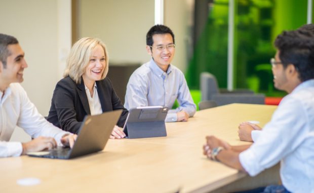 group of people sitting around table with laptops looking at each other