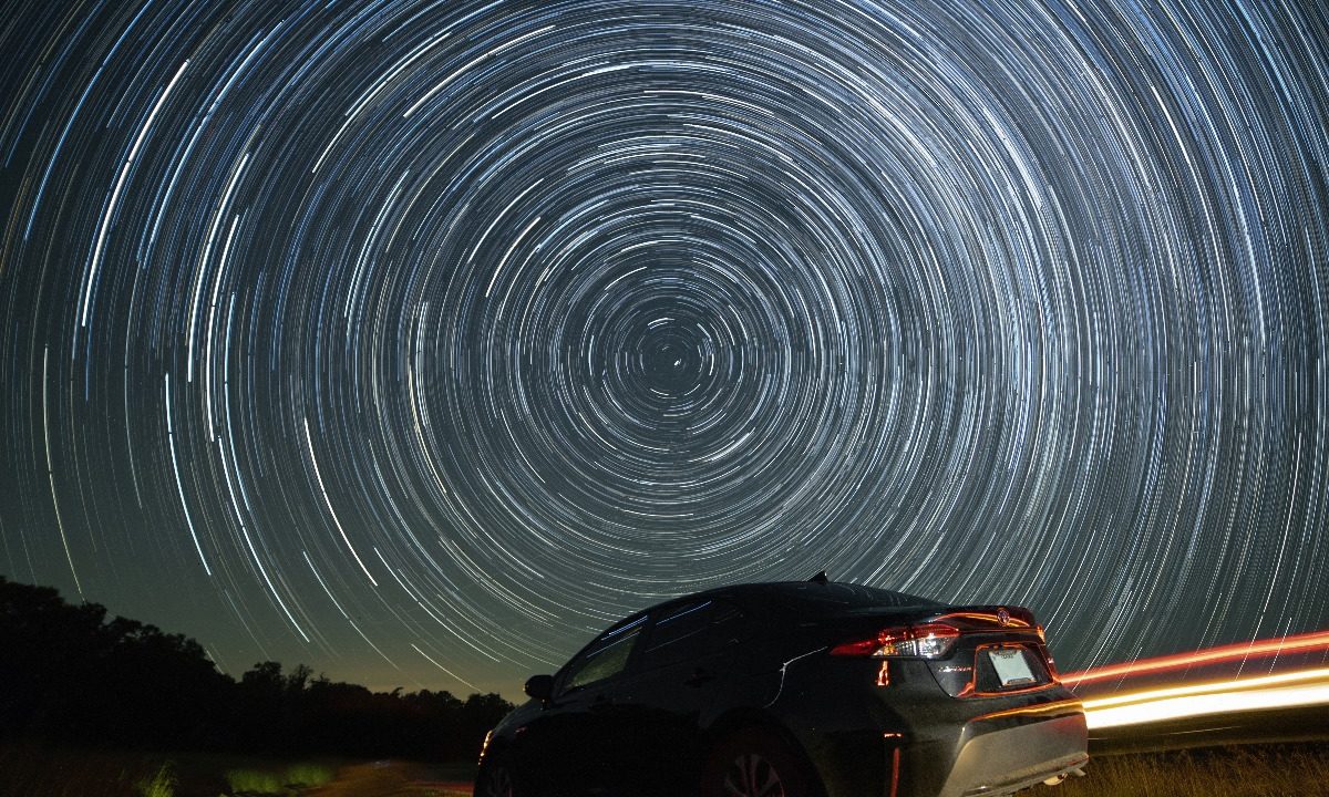 long exposure of night sky which makes stars appear like swirling lights with car in front