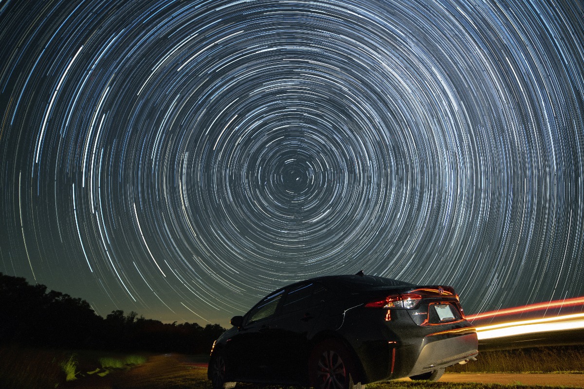 long exposure of night sky which makes stars appear like swirling lights with car in front