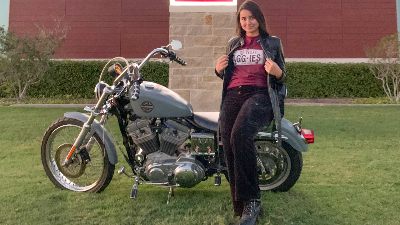 young woman wearing Aggie T-shirt and standing in front of motorcycle