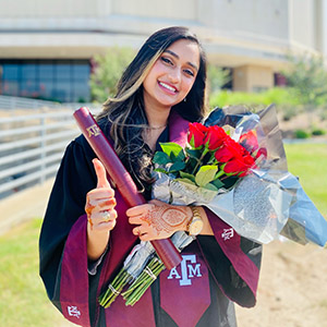 young woman wearing graduation robe and smiling while standing outside on Texas A&M University campus