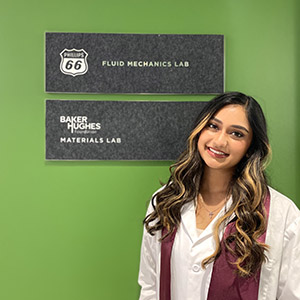 young woman in lab coat stands in front of materials lab sign