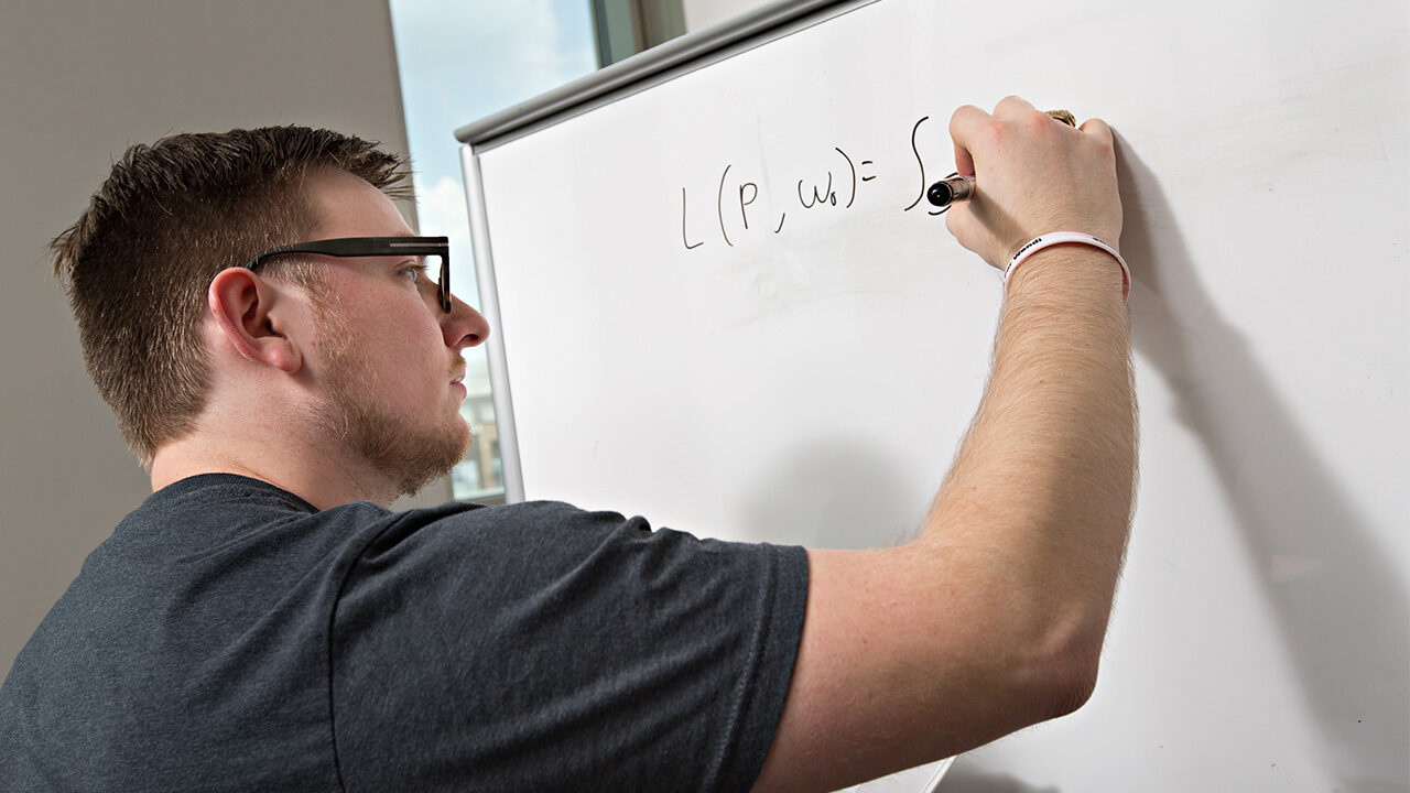 A student writing math equations on a whiteboard