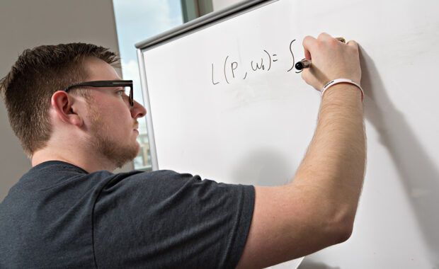 A student writing math equations on a whiteboard