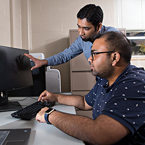 Ingenium blogger Vishal Kandala working on a computer while another male graduate student points to the monitor