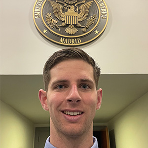 Austin Kees in front of the Madrid Embassy of the United States of America logo