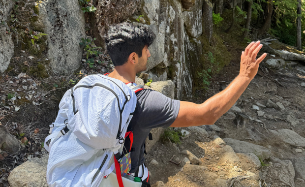 A student wearing a backpack hiking down a steep rocky hill.