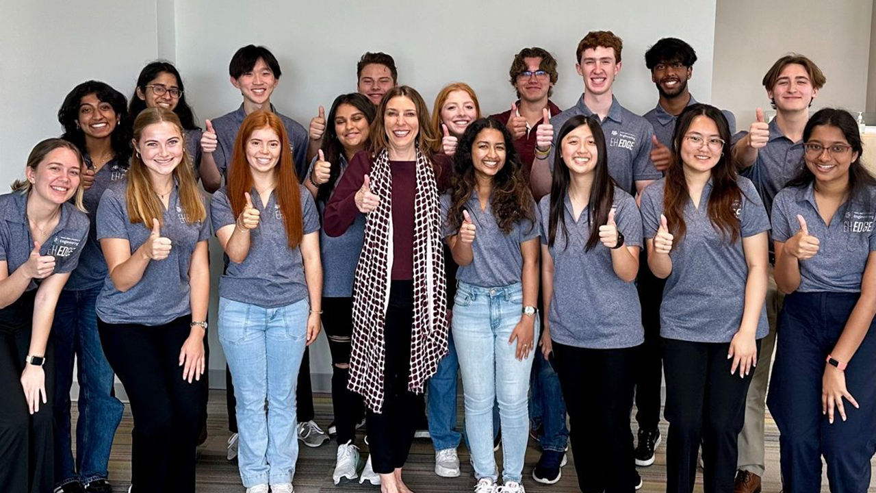 Group photo of EH Edge students smiling, wearing grey polo shirts, displaying thumbs up gesture