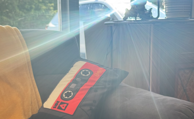 Sunbeam peering through a window, landing on a couch with a pillow shaped like a cassette tape.