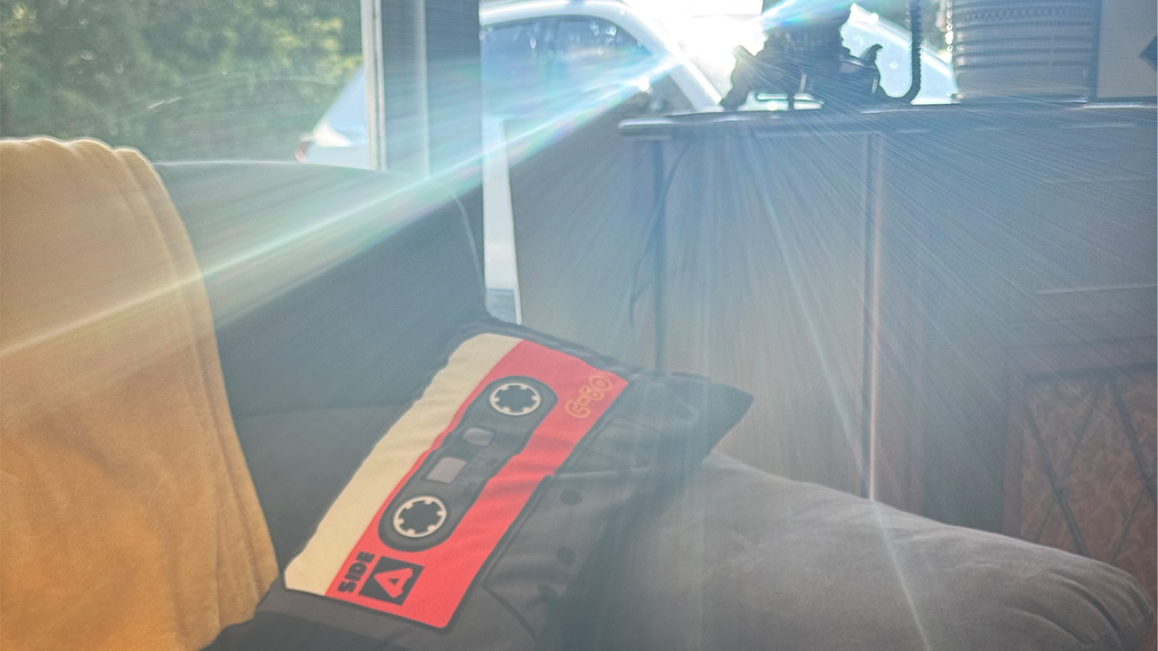 Sunbeam peering through a window, landing on a couch with a pillow shaped like a cassette tape.